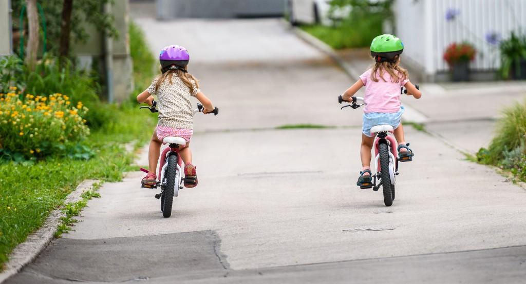 Két bukósisakos kislány háttal kétkerekű biciklit teker