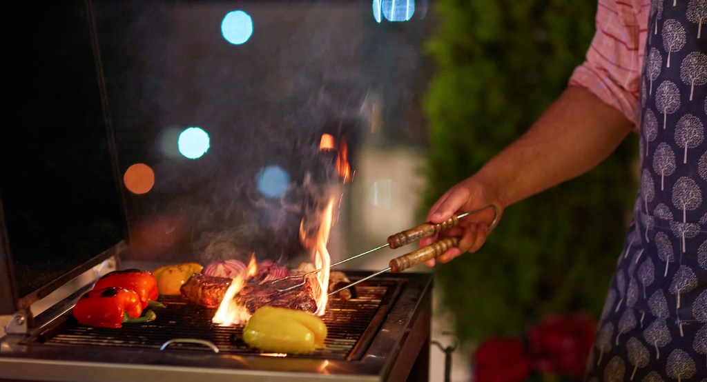 Grillen felcsapó láng, ahol szaftos húst süt egy férfi