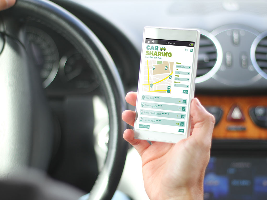 A volánnál ülő kezében mobiltelefont tart és applikációt néz